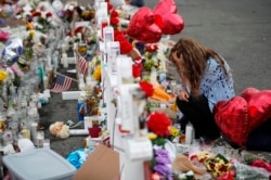 Gloria Garces kneels in front of crosses at a makeshift memorial near the scene of a mass shooting at a shopping complex, Aug. 6, 2019, in El Paso, Texas.