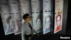 Una mujer camina junto a pancartas de billetes de bolívares venezolanos que se exhiben en el edificio del Banco Central de Venezuela en Caracas, el 23 de mayo de 20217.