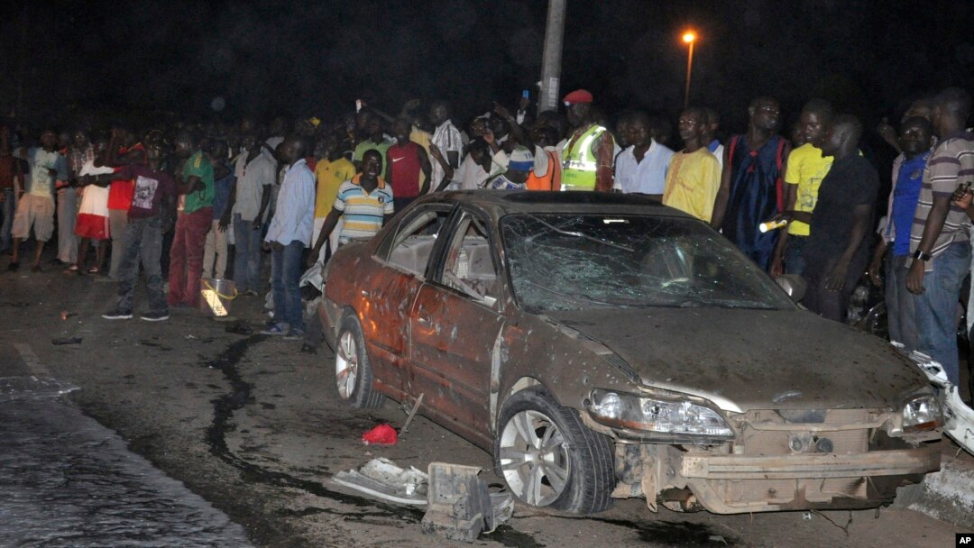 Warga berkumpul di dekat sebuah mobil yang hancur karena ledakan bom di Abuja, Nigeria (1/5).