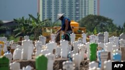 Seorang pekerja menyiram makam-makam baru korban virus corona (Covid-19) di pemakaman Keputih di Surabaya, Jawa Timur, 15 Juli 2020. (Foto: AFP)