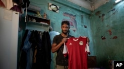 In this May 9, 2020 photo, 28-year-old defender Mahrous Mahmoud holds up his Egyptian national football team jersey he trains with, inside his home, in Manfalut, a town 350 kilometers (230 miles) south of Cairo in the province of Assiut, Egypt.
