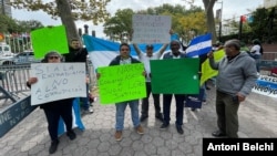 Un grupo de hondureños posan para la Voz de América frente al edificio de las Naciones Unidas en Nueva York con carteles de rechazo a la política de Xiomara Castro por cancelar el tratado de extradición con EEUU.