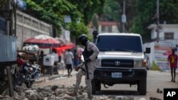 Polisi tampak membereskan susunan batu yang digunakan untuk memblokade jalan seusai protes yang dilakukan para warga di Port-au-Prince yang menyuarakan lemahnya sistem keamanan di Haiti pada 18 Oktober 2021. (Foto: AP/Joseph Odelyn)