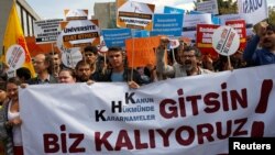 FILE - Demonstrators hold signs in front of the High Education Board during a protest against the suspension of academics from universities following a post-coup emergency decree, in Ankara, Turkey, Sept. 22, 2016. The sign in the foreground reads "Let the emergency decrees go. We are remaining."