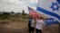 FILE - Israelis hold American and Israeli flags with the new U.S. Embassy in the background in Jerusalem, May 14, 2018. Seventy years after Israel's founding, images of victory and violence showcased the contradictions that bedevil the Jewish state.