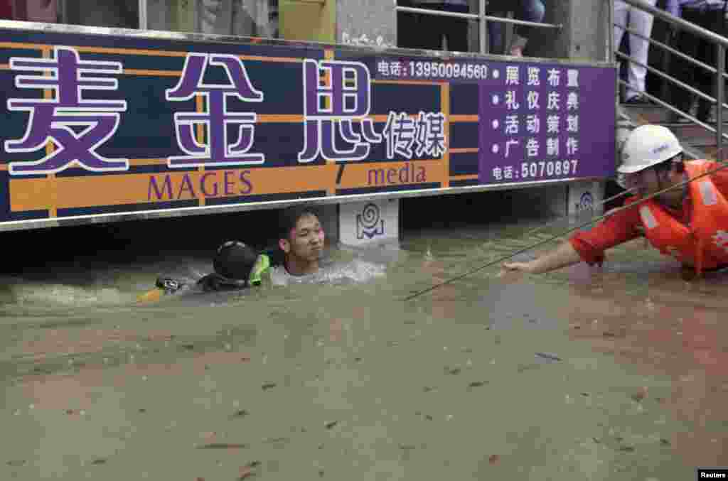 Seorang penyelam (kiri) menyelamatkan seorang pria yang terjebak banjir selama 8 jam di komplek pertokoan setelah hujan deras melanda Xiamen, provinsi Fujian, Cina.