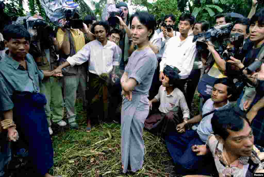 Aung San Suu Kyi is surrounded by security guards and newsmen as she walks out of her lakeside house in Rangoon, Burma, Juy 14, 1995. 