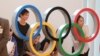 Orang-orang foto di depan logo Olimpiade di Bandara Internasional Haneda di Tokyo, Jepang, Kamis, 8 Juli 2021. (AP Photo/Koji Sasahara)