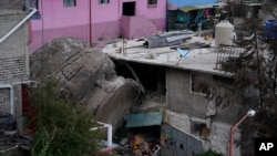 A boulder that plunged from a mountainside rests among homes in Tlalnepantla, on the outskirts of Mexico City, when a mountain gave way on Sept. 10, 2021. 