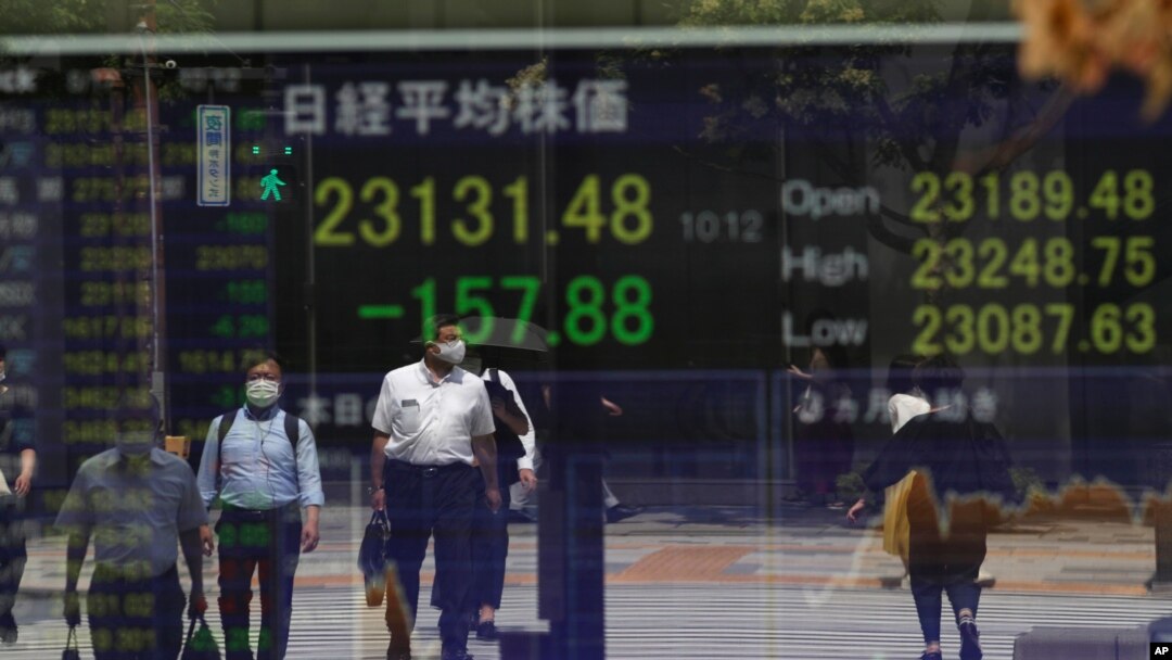 Orang-orang menunggu di persimpangan lalu lintas, tercermin pada monitor yang menunjukkan indeks Nikkei 225 Jepang di sebuah perusahaan sekuritas di Tokyo pada hari Senin, 17 Agustus 2020. (Foto: AP)