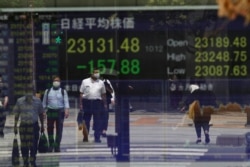 People wait at a traffic intersection, reflected on a monitor showing Japan's Nikkei 225 index at a securities firm in Tokyo on Aug. 17, 2020.