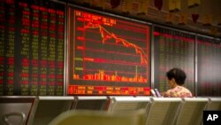 A Chinese investor uses her smartphone as she monitors stock prices at a brokerage house in Beijing, Friday, July 6, 2018. President Donald Trump made clear Thursday that U.S. tariffs against Chinese imports will take effect early Friday and that he's prepared to sharply escalate a trade war between the world's two biggest economies.