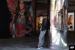 FILE - A man wearing Nike shoes uses his smartphone near an advertisement for U.S. lingerie maker Victoria's Secret, in Beijing, China, May 21, 2019.