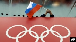 FILE - A Russian flag is held above the Olympic Rings at Adler Arena Skating Center during the Winter Olympics in Sochi, Russia on Feb. 18, 2014. (AP Photo/David J. Phillip, File)