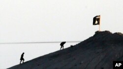 Dalam foto yang diambil dengan lensa telefoto, terlihat di pinggiran kota Suruc di perbatasan antara Turki dan Suriah, militan ISIS dengan bendera kelompok ini di sebuah puncak pegunungan di sisi timur Suruc.