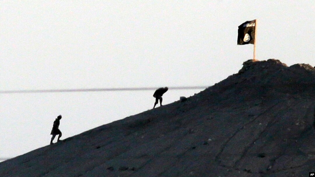 FILE - In this image shot with an extreme telephoto lens and through haze from the outskirts of Suruc at the Turkey-Syria border, militants with the Islamic State group are seen after placing their group's flag on a hilltop at the eastern side of the town