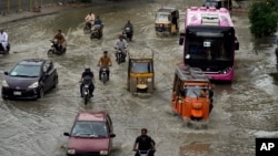 FILE- Motorcyclists and cars drive through a flooded road caused by heavy monsoon rainfall in Karachi, Pakistan, July 30, 2024.