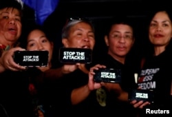 FILE - Journalists, including Rappler CEO Maria Ressa, raise their smartphones with words "STOP THE ATTACKS!" in a rally for press freedom in Quezon City, Philippines, Feb. 15, 2019.