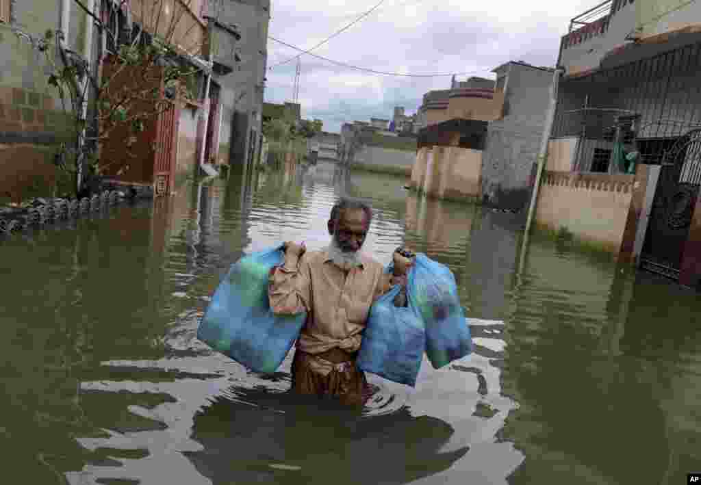 A man carries goods as he wades through flooded street after heavy monsoon rains, in Karachi, Pakistan.
