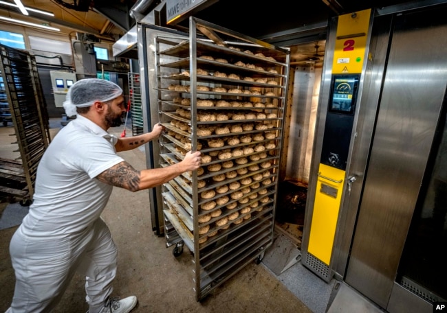 An employee pushes bread rolls into one of the gas heated ovens in the producing facility in Cafe Ernst in Neu Isenburg, Germany, Monday, Sept. 19, 2022. Andreas Schmitt, head of the local bakers' guild, said some small bakeries are contemplating giving up due to the energy crisis. (AP Photo/Michael Probst)