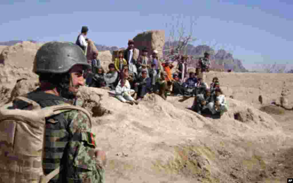 An Afghan soldier stands guard as local children watch Secretary Gates' delegation walk by in Tabin Village