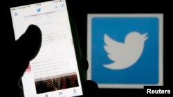 FILE - A man reads tweets on his phone in front of a displayed Twitter logo in Bordeaux, southwestern France, March 10, 2016. 