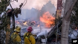 Firefighters try to extinguish the flames at a burning house as the South Fire burns in Lytle creek, San Bernardino County north of Rialto, Calif., Aug. 25, 2021.