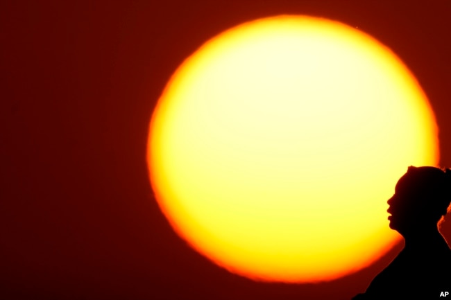 FILE - A woman is silhouetted against the setting sun as triple-digit heat indexes continue in the Midwest, Aug. 20, 2023, in Kansas City, Mo. Earth is exceeding its “safe operating space for humanity” a new study said. (AP Photo/Charlie Riedel, File)