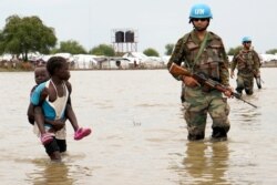 A girl holding a child walks past UN peacekeepers, after heavy rains and floods forced hundreds of thousands of people to leave their homes, in the town of Pibor, Boma state, South Sudan, Nov. 6, 2019.