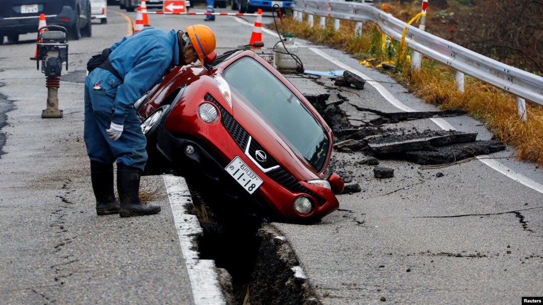 Spasilac gleda u automobil zarobljen u pukotini na putu nastaloj tokom zemljotresa u blizini Anamiza, Japan, 3. januara 2023.