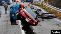 A worker looks at a car stuck on a cracked road in the aftermath of an earthquake, near Anamizu, Japan, Jan. 3, 2024.
