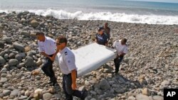 FILE - French police officers carry a piece of debris, the first trace of Malaysia Airlines Flight 370, in Saint-Andre, Reunion Island, July 29, 2015. Oceanographers have been analyzing the wing flaps from La Reunion and Tanzania in the hope of identifying a possible new search area through drift modeling. 