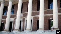 مردی نشسته بر پله های کتابخانه دانشگاه هاروارد در حال تماس تلفنی ماسک به صورت زده است. ۲۶ ژوئن ۲۰۲۰