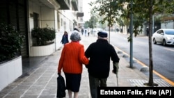 FILE - A couple walk on a sidewalk in Santiago, Chile, Wednesday on May 3, 2017. 