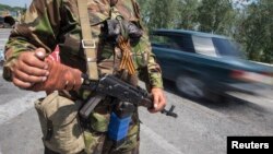 An armed pro-Russian separatist with attached orange ribbon of St. George, a symbol widely associated with pro-Russian protests in Ukraine, stands guard at a road checkpoint outside the eastern Ukrainian city of Luhansk, June 8, 2014.