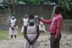 FILE - A teacher checks students for fever at Lagos State Model School in Lagos, Nigeria, Aug. 4, 2020.