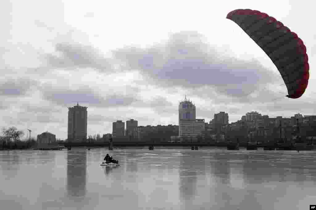 A man enjoys a ride on a sled pulled by a kite on the frozen river of Kalmius in Donetsk, Ukraine.