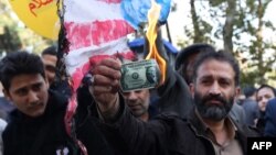 A protester burns a dollar banknote during a demonstration outside the former US embassy in the Iranian capital Tehran. Nov. 4, 2018.