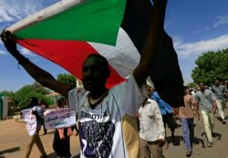 A Sudanese man carries the national flag as protesters march in a demonstration to mark the anniversary of a transitional power-sharing deal with demands for quicker political reforms in Khartoum, Sudan, Aug. 17, 2020.
