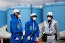 FILE - Workers are seen in front of storage tanks for radioactive water at the tsunami-crippled Fukushima Daiichi nuclear power plant in Okuma town, Fukushima prefecture, Japan, Feb. 18, 2019.