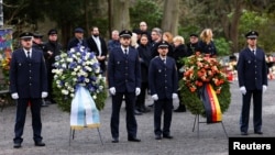 Police officers and members of an honor guard await the arrival of politicians next to wreaths at a memorial for two people, including a child, killed in a knife attack earlier in the week in Aschaffenburg, Germany, Jan. 26, 2025.