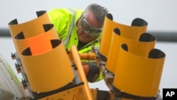 A worker copes with strong winds while repairing a traffic light, March 2, 2018, in Hull, Massachusetts.