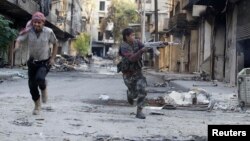 FILE - Mohammad (R), a 13 year-old fighter from the Free Syrian Army, aims his weapon as he runs from snipers loyal to the Syrian regime in Aleppo's Bustan al-Basha district October 29, 2013.