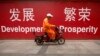 FILE - A maintenance worker rides a scooter past banners reading "Development" and "Prosperity" in English and Chinese on a street in central Beijing, July 15, 2015.