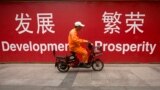 FILE - A maintenance worker rides a scooter past banners reading "Development" and "Prosperity" in English and Chinese on a street in central Beijing, July 15, 2015.