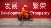 FILE - A maintenance worker rides a scooter past banners reading "Development" and "Prosperity" in English and Chinese on a street in central Beijing, July 15, 2015.