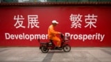 FILE - A maintenance worker rides a scooter past banners reading "Development" and "Prosperity" in English and Chinese on a street in central Beijing, July 15, 2015.