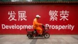 FILE - A maintenance worker rides a scooter past banners reading "Development" and "Prosperity" in English and Chinese on a street in central Beijing, July 15, 2015.