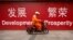 FILE - A maintenance worker rides a scooter past banners reading "Development" and "Prosperity" in English and Chinese on a street in central Beijing, July 15, 2015.
