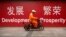 FILE - A maintenance worker rides a scooter past banners reading "Development" and "Prosperity" in English and Chinese on a street in central Beijing, July 15, 2015.